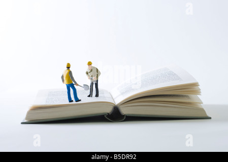 Les travailleurs de la construction miniature debout sur un livre ouvert Banque D'Images