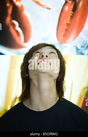 Jeune homme debout sous l'image de l'affiche de la pendaison de pinces de homard, looking up Banque D'Images