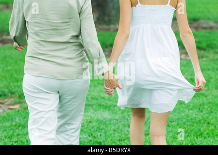 Mère et fille la marche à l'extérieur, tenant les mains, cropped vue arrière Banque D'Images