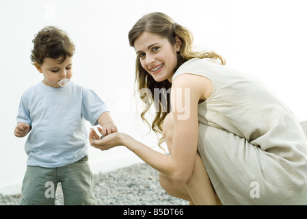 Femme accroupie, smiling over Shoulder toddler prend de sa main de galets Banque D'Images