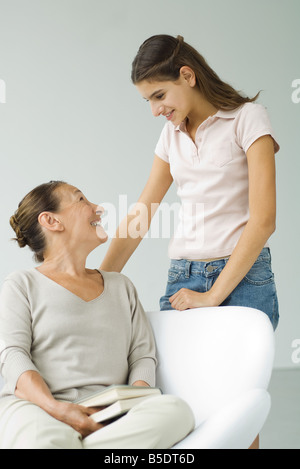 Grand-mère assise dans une chaise, tenue de livre, petite-fille de l'adolescence se tiennent à proximité Banque D'Images