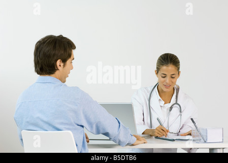 Femme médecin assis en face de patient de sexe masculin à 24, écrit des notes Banque D'Images