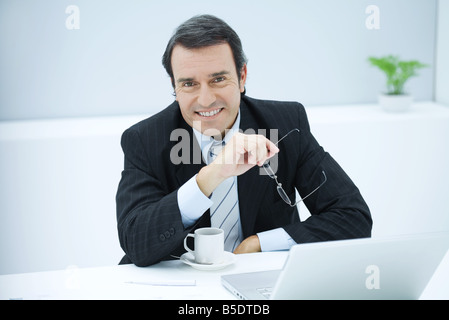 Businessman sitting at desk with coffee cup, smiling at camera Banque D'Images