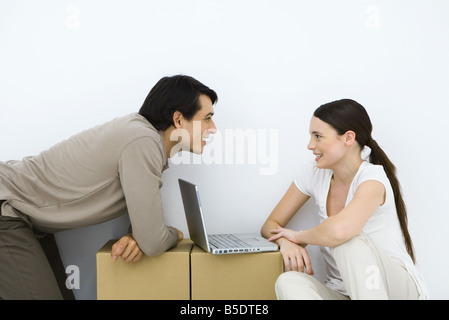 Couple sitting at desk with laptop computer de fortune entre eux, smiling at each other Banque D'Images