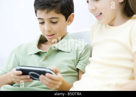 Frère et sœur siégeant ensemble, boy playing handheld video game Banque D'Images