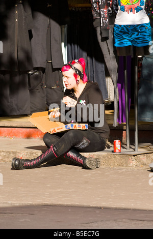 London Camden Lock Market jolie fille punk cheveux rose queue partie bottes tête rasée percés bouche mange pizza by boutique Banque D'Images