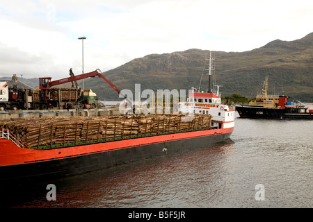 Un bateau de marchandises d'être chargé de sciage par grue à quai à Kyle of Lochalsh avec un bateau qui passe en arrière-plan. Banque D'Images