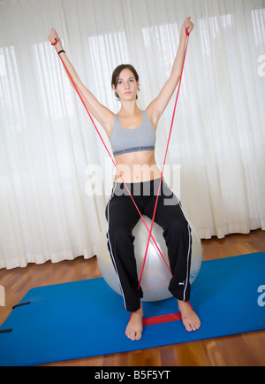 Jeune femme faisant des exercices avec theraband assise sur boule d'exercice Banque D'Images