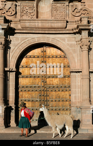 Femme Quechua en costume traditionnel avec un lama en passant devant une porte de l'église à Cusco Banque D'Images
