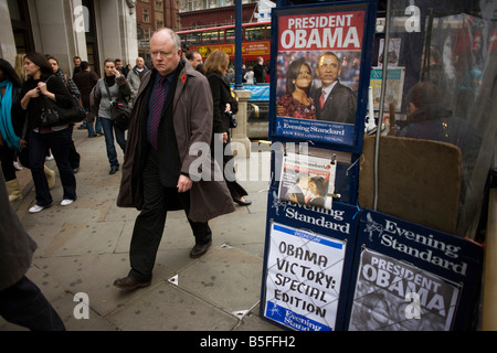 Les passants dans le quartier londonien de Oxford Circus prendre dans morning news de Barack Obama's victoire historique sur les manchettes de journaux Banque D'Images