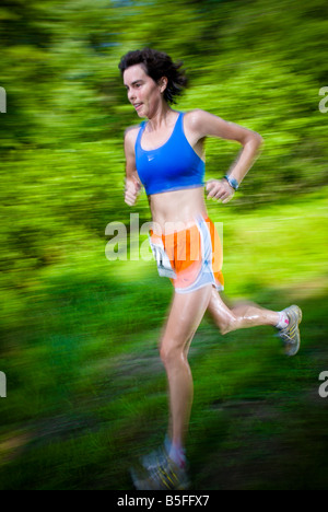 Une coureuse participant à une course run trail Xterra à travers un champ tout en tenant une bouteille d'eau jaune Banque D'Images