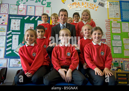 Un directeur de l'école primaire avec des élèves en uniforme rouge sweat-shirts dans une salle de classe Banque D'Images