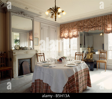 Grand miroir au-dessus de cheminée en gris salle à manger avec fenêtres et stores ruched à blanc et vérifié sur table ovale Banque D'Images