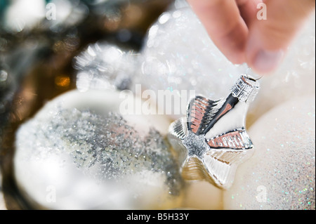 Ornements de Noël blanc et argent recueilli dans un bol en argent avec une femme main tenant l'un des ornements Banque D'Images