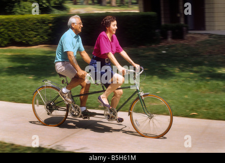 Senior Hispanic couple rides tandem on sidewalk Banque D'Images