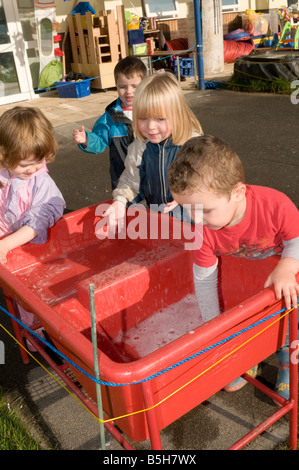 Quatre jeunes enfants dans les jardins d'enfants garderie maternelle jouant avec l'eau à l'extérieur Banque D'Images