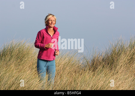 Jeune femme blonde à l'extérieur. La course à travers l'herbe haute. Banque D'Images