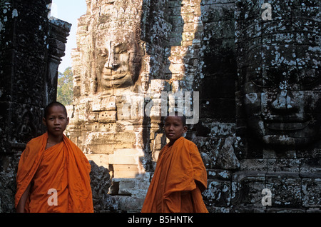 Deux jeunes moines novices se tenir en face d'énormes visages gravés dans la pierre à Bayon, Angkor Thom, Angkor, Cambodge temple Banque D'Images