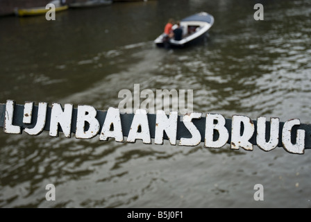 Un canot envahit l'un des nombreux canaux d'Amsterdam. Dans l'avant-plan est un signe pour Lunbaansbrug, une rue de Jordaan. Banque D'Images