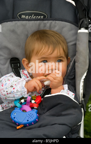 Fille bébé enfant assis assis dans une poussette à mâcher sur un anneau de dentition Banque D'Images