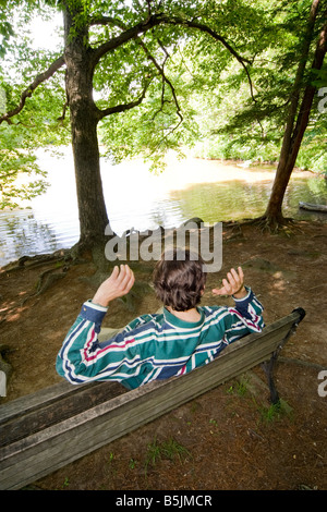 Homme assis sur un banc dans un parc à côté d'un modèle de l'étang publié Banque D'Images