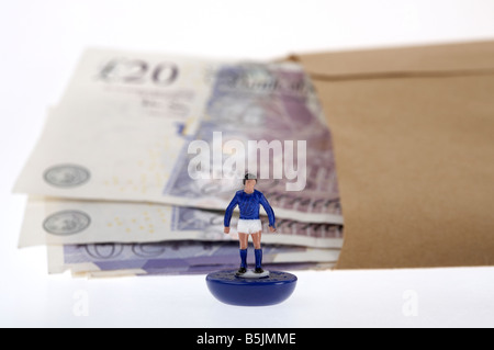 Liasse de billets de banque de 20 livres sterling l'argent dans une enveloppe de papier brun derrière footballeur jouet Banque D'Images
