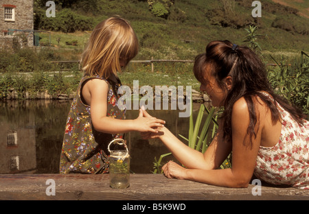 Le collage de la mère avec sa fille de trois ans à côté d'un étang dans la campagne, Cornwall, UK Banque D'Images