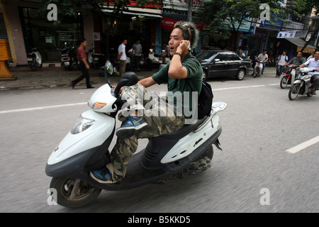 Un homme parle sur son téléphone cellulaire au volant de sa mobylette à Hanoi, Vietnam. Banque D'Images