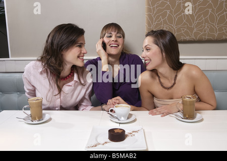 Trois femmes connaissant leur café avec un parler sur un téléphone cellulaire. Banque D'Images