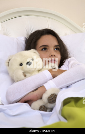 Une petite fille dans le lit avec un ours en peluche Banque D'Images