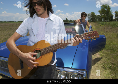 Deux hommes avec une voiture bleue et en jouant de la guitare Banque D'Images