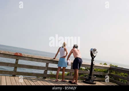 Jeune couple près d'un périphérique binoculaire sur une promenade à la plage à la recherche sur la clôture à l'eau Banque D'Images