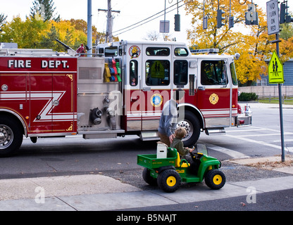 Père et fils regarder fire engine dans petite ville, USA, sur un jour d'automne. Le garçon est monté sur un camion jouet. Banque D'Images