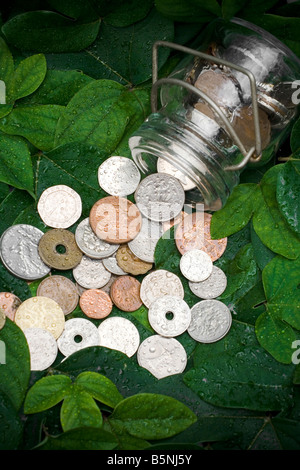 Pièces antiques déversés par un récipient en verre sur Vert feuilles Banque D'Images