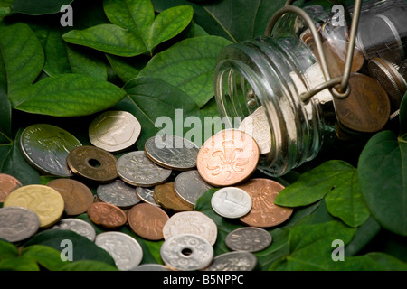 Pièces antiques déversés par un récipient en verre sur Vert feuilles Banque D'Images