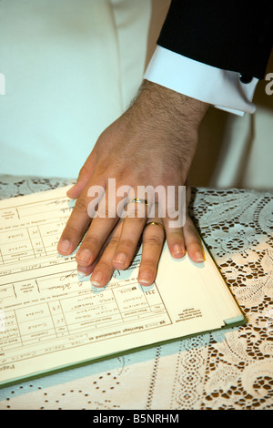 Mariés jeunes mariés mari et femme se tenant la main sur le registre de mariage pendant la cérémonie du mariage en UK Banque D'Images