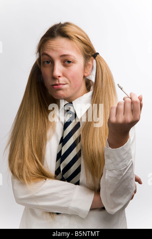 Le port de l'uniforme d'écolière adolescents fumeurs cigarette avec ses cheveux blonds en bouquets, UK Banque D'Images