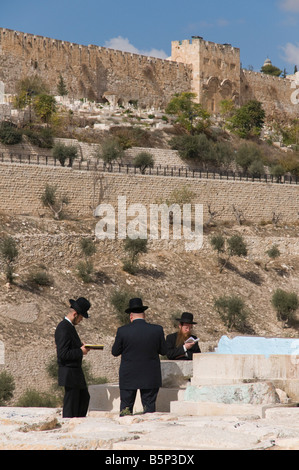 Mont des Oliviers Jérusalem Israël trois juifs orthodoxes priant à un tombeau avec Golden Gate de bkgd Banque D'Images