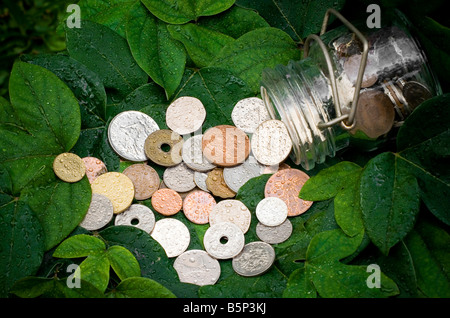 Pièces antiques déversés par un récipient en verre sur Vert feuilles Banque D'Images