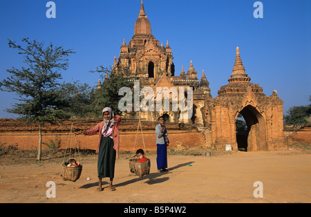 Une femme porte ses deux enfants dans des paniers à l'avant du Tayok Pye Temple à Bagan, Birmanie ou Myanmar Banque D'Images