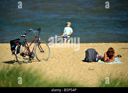 Woman relaxing on beach alors que jeune garçon joue dans le sable avec un chat Banque D'Images