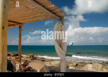 Un voyageur salons dans une cabane sur la plage de Little Stirrup Cay. Bateau de croisière majesté des mers peut être vu dans la distance. Banque D'Images