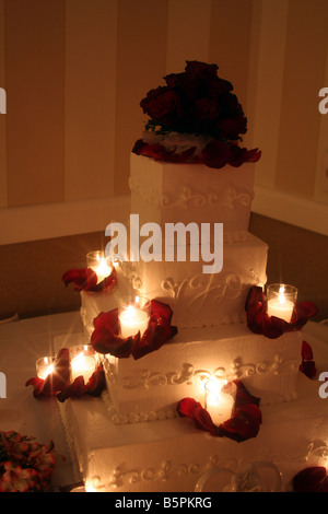 Un beau gâteau de mariage avec des roses rouges sur le dessus et des bougies allumées autour du cake affiché pour une réception de mariage Banque D'Images
