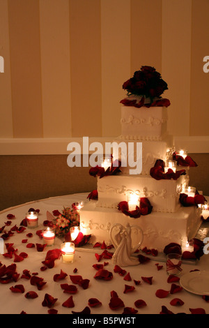 Un beau gâteau de mariage avec des roses rouges sur le dessus et des bougies allumées autour du cake affiché pour une réception de mariage Banque D'Images