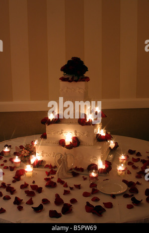 Un beau gâteau de mariage avec des roses rouges sur le dessus et des bougies allumées autour du cake affiché pour une réception de mariage Banque D'Images