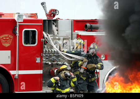 Trois pompiers l'obtention d'un prêt d'un hoseline camion à incendie lors d'un incendie lors d'une démonstration de la sécurité incendie Banque D'Images