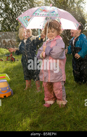 Les jeunes enfants dans une crèche garderie jouer avec de l'eau vaporisée et parapluie à l'extérieur dans le jardin. UK Banque D'Images