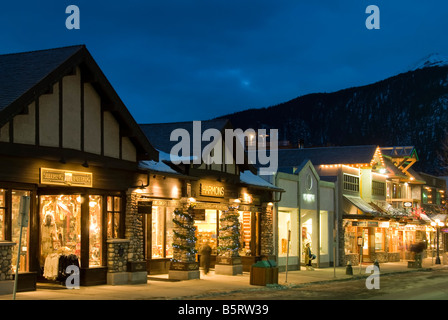 Boutiques le long de l'avenue Banff, au crépuscule, la ville de Banff, Banff National Park, Alberta, Canada. Banque D'Images