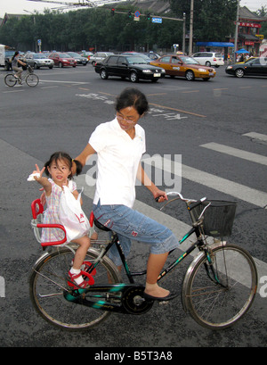 Une jeune fille d'équitation vagues tandis que sur un vélo avec sa mère à Pékin, Chine Banque D'Images