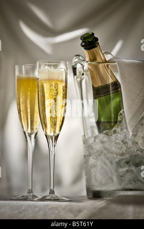 Deux verres de champagne avec une bouteille de champagne dans un seau de glace sur un tissu blanc fond drapé Banque D'Images